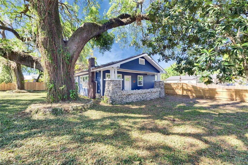 A blue house with a stone porch and chimney sits under a large oak tree — 1021 E 25TH AVENUE, TAMPA, FL