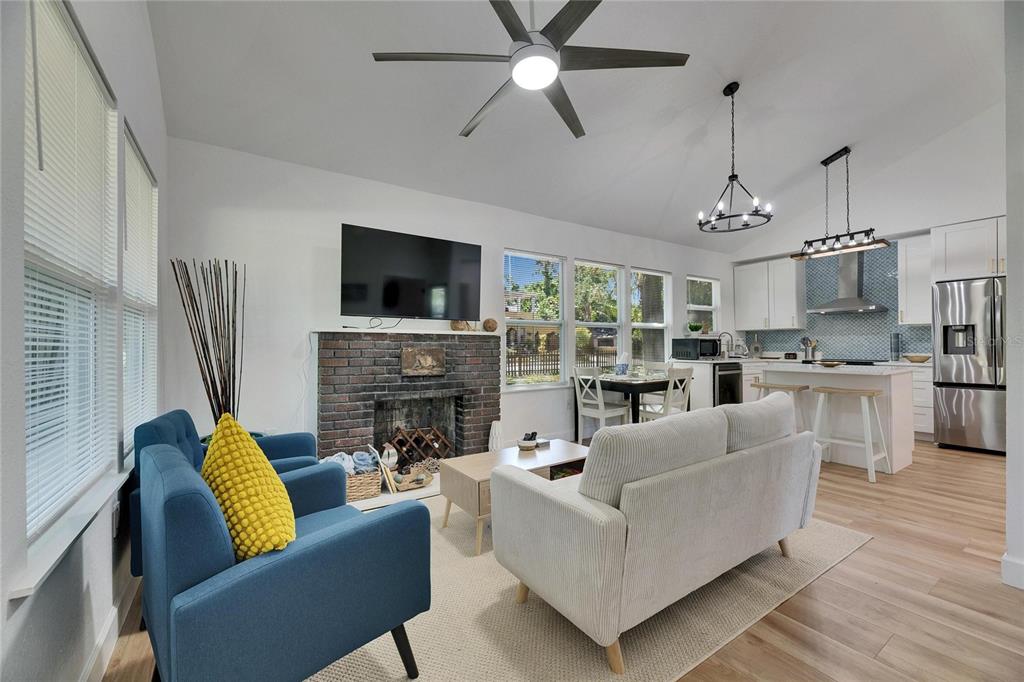 A living room with a brick fireplace, blue armchairs, a white sofa, and an open kitchen — 1021 E 25TH AVENUE, TAMPA, FL