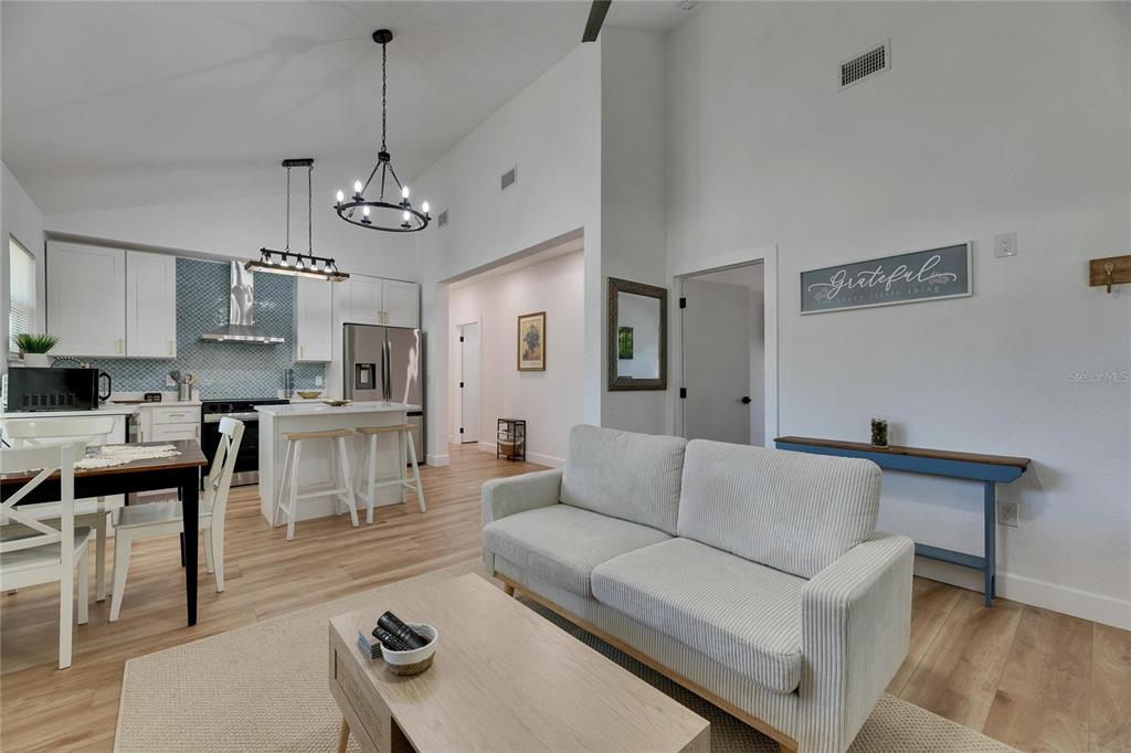 An open-concept living room and kitchen featuring white cabinetry, light wood flooring, and vaulted ceilings — 1021 E 25TH AVENUE, TAMPA, FL
