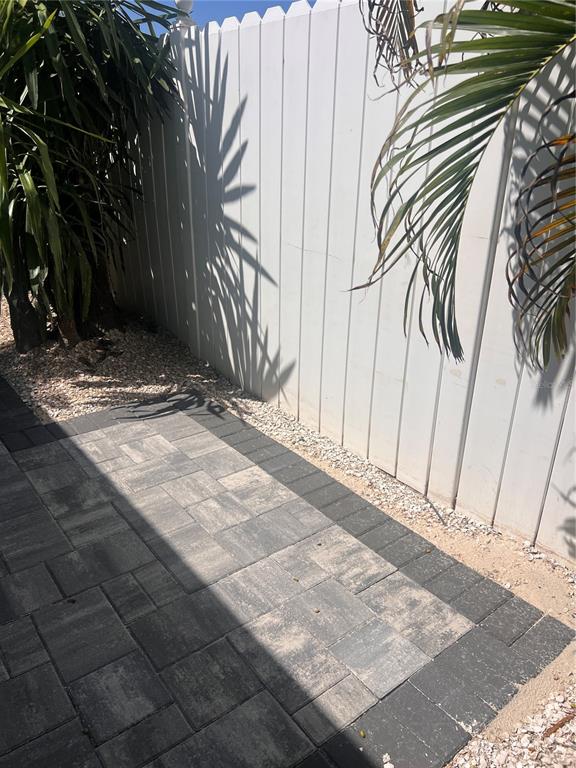A paved patio area sits beside a white vinyl fence and some tropical plants — 40 82ND AVENUE S Unit `1, TREASURE ISLAND, FL