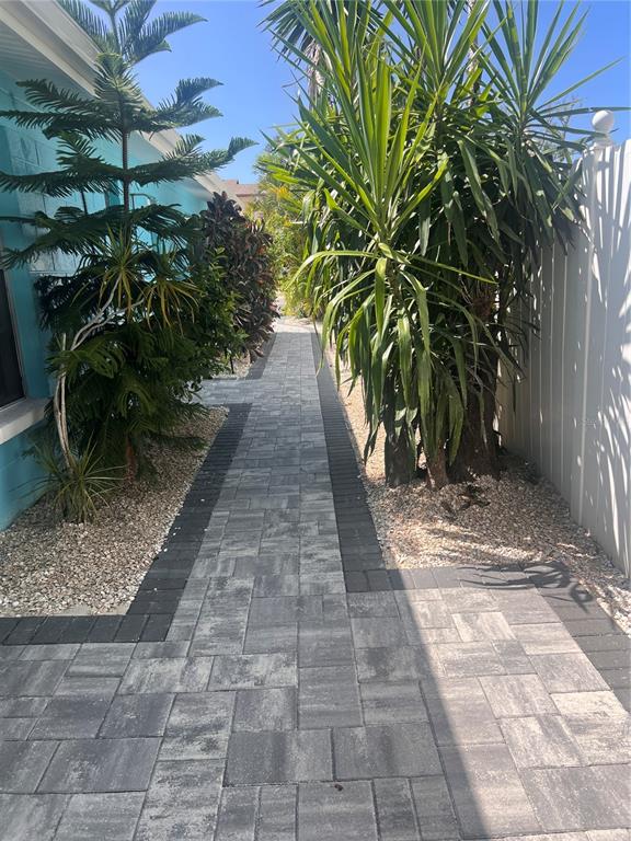 A paved walkway leads between a blue house and a white fence with tropical plants — 40 82ND AVENUE S Unit `1, TREASURE ISLAND, FL
