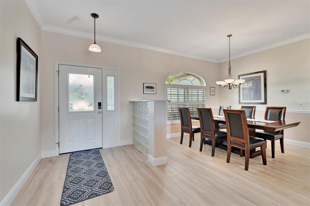 A dining area with a glass block partition, light wood floors, and a front entryway — 6738 PEACH TREE CREEK ROAD, BRADENTON, FL