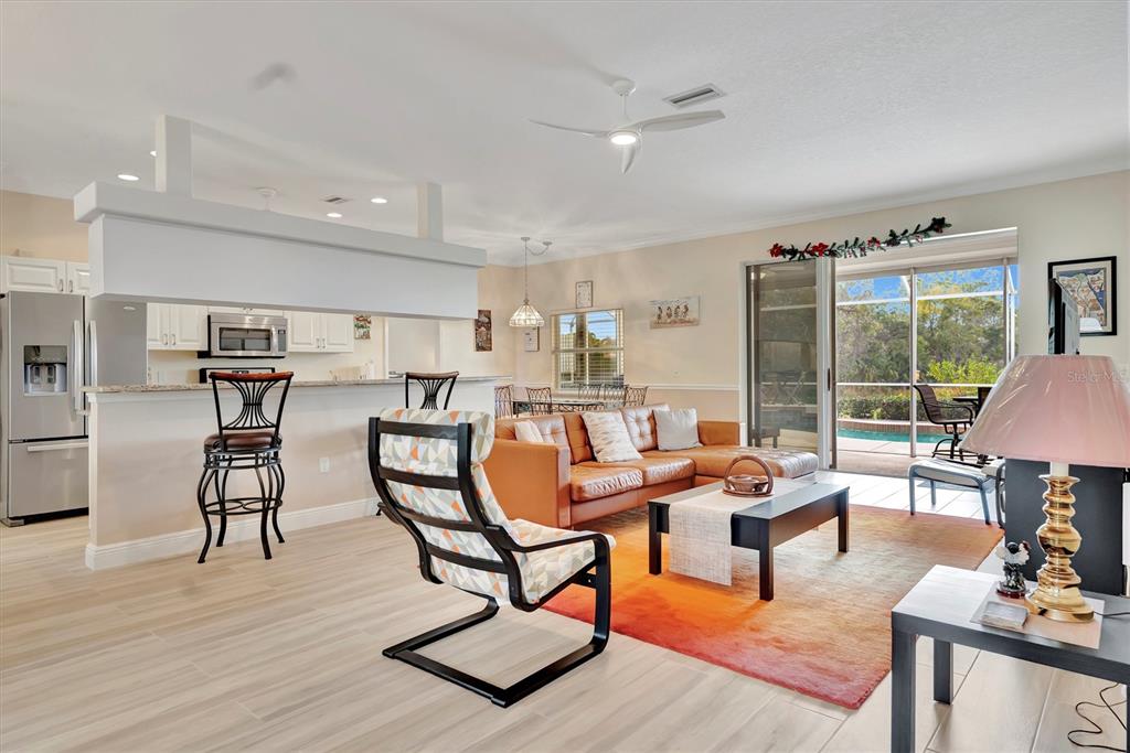 An open-concept living room and kitchen feature light tile flooring, a leather sofa, and pool views — 6738 PEACH TREE CREEK ROAD, BRADENTON, FL
