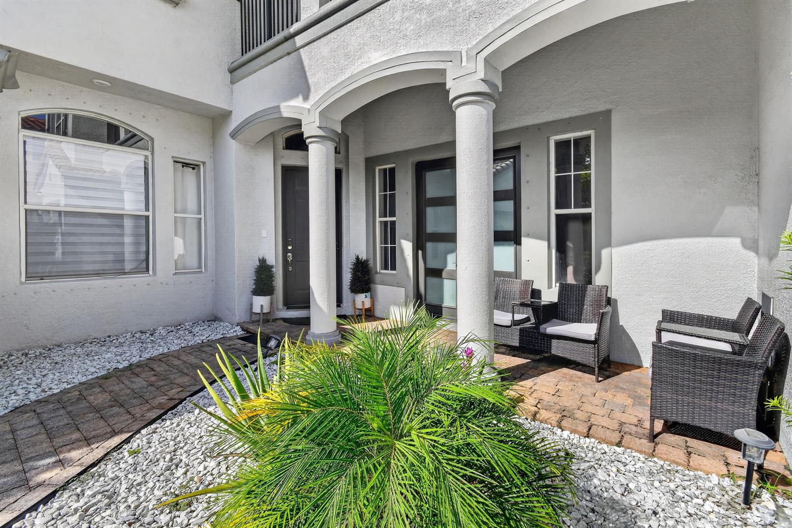A paved entryway features white columns, a dark front door, and outdoor wicker seating — 700 Cresta Circle, West Palm Beach FL 33413, WEST PALM BEACH, FL