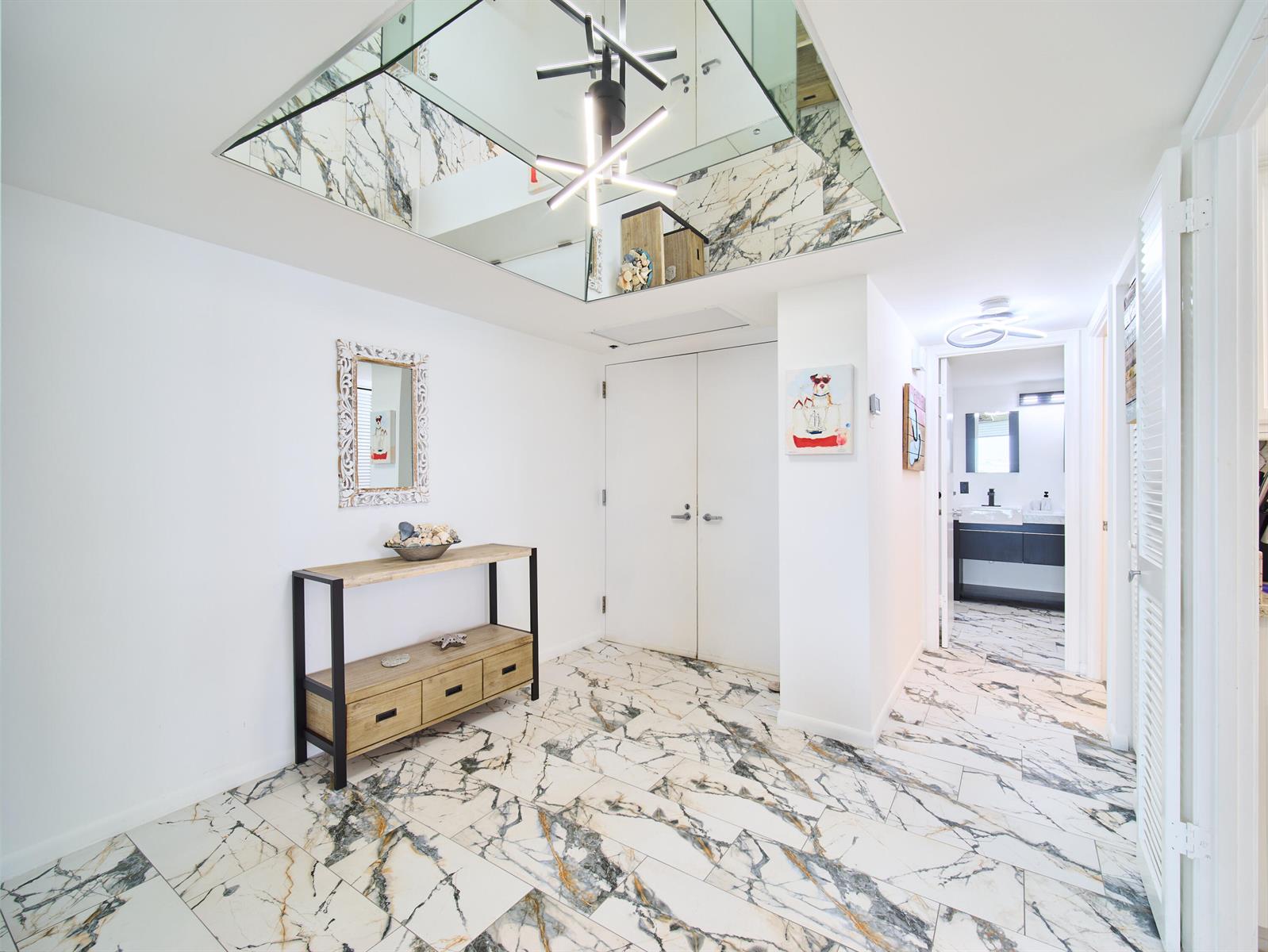 A bright entryway features marble-patterned tile flooring, a mirrored ceiling, and a modern console table — 5550 N Ocean Drive # 9D, Singer Island FL 33404, SINGER ISLAND, FL
