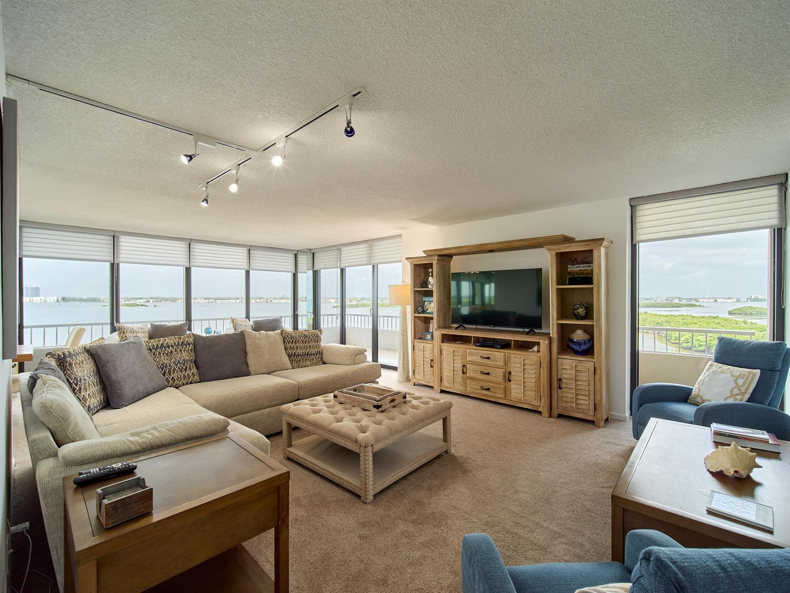 A living room with a large sectional, wooden entertainment center, and floor-to-ceiling windows overlooking water — 5550 N Ocean Drive # 9D, Singer Island FL 33404, SINGER ISLAND, FL