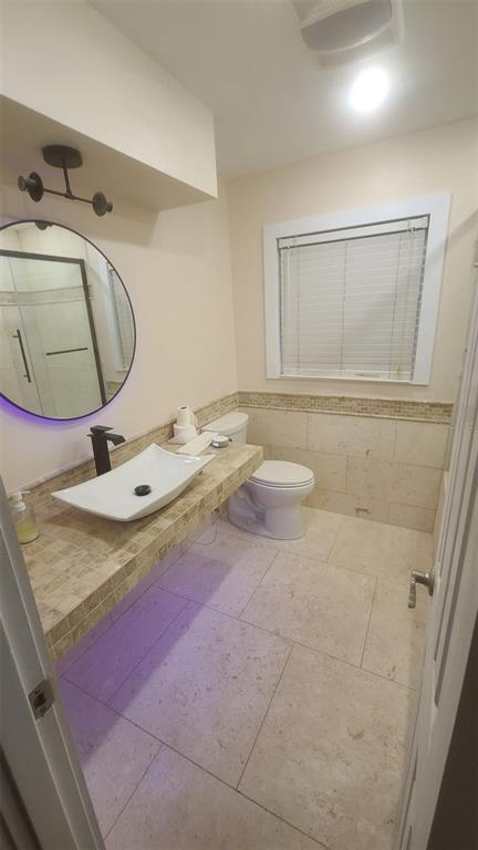 A bathroom features a vessel sink on a tiled vanity, a round mirror, and tile flooring — 2018 MARILYN AVENUE, WINTER HAVEN, FL