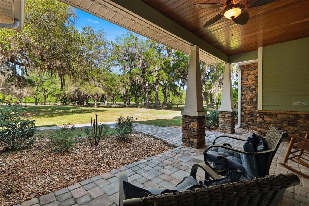 A covered stone-paved porch features a wood-paneled ceiling, a ceiling fan, and outdoor seating — 12501 N US HIGHWAY 27, OCALA, FL