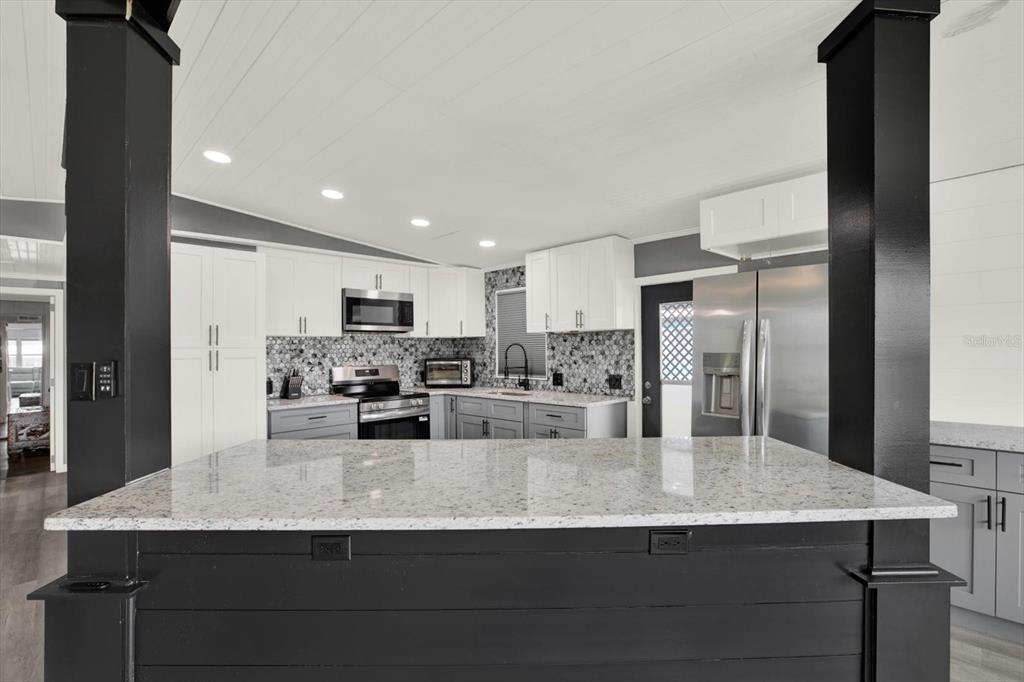 A kitchen features a granite-topped island, white upper cabinets, gray lower cabinets, and black pillars — 8431 MOONLIGHT AVENUE, BROOKSVILLE, FL