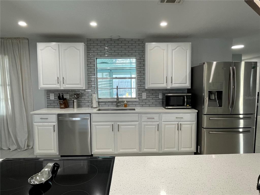 A kitchen features white cabinets, stainless steel appliances, and a gray subway tile backsplash — 1695 N BANANA RIVER DRIVE, MERRITT ISLAND, FL