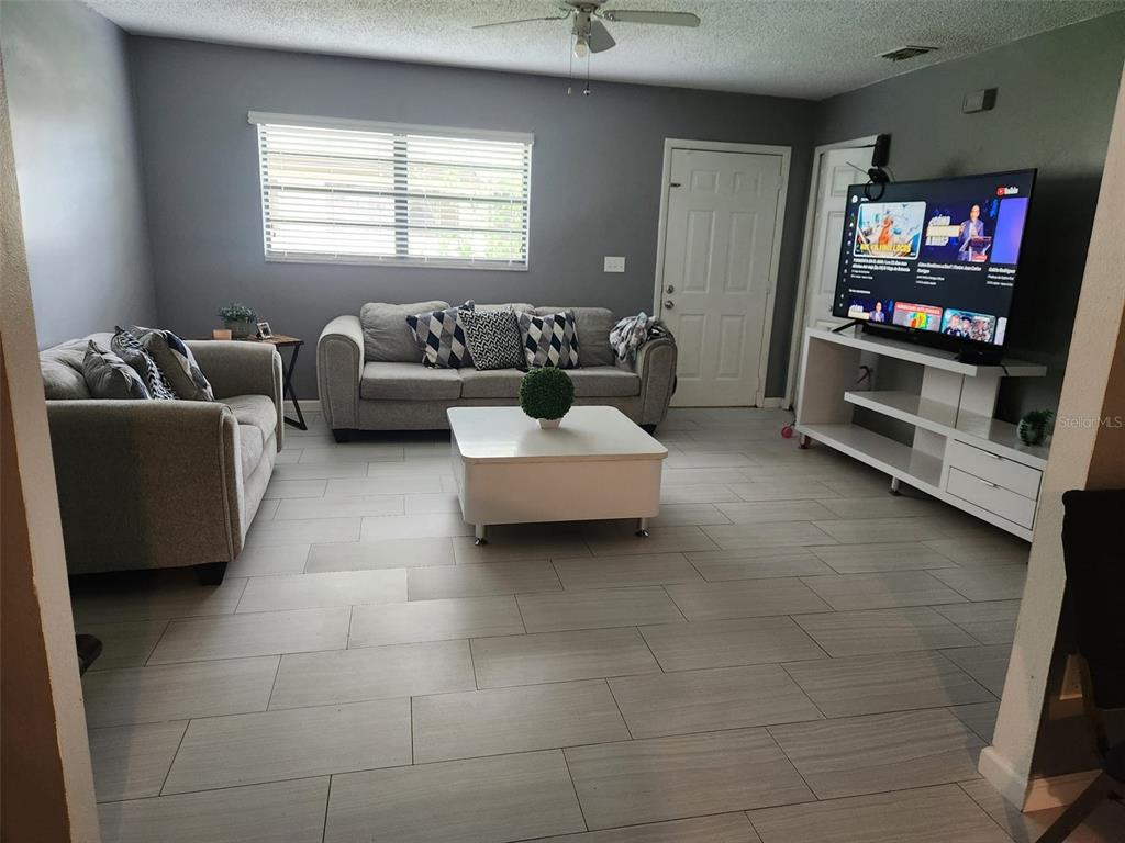 A living room features gray walls, light tile flooring, a sofa, and a television console — 1695 N BANANA RIVER DRIVE, MERRITT ISLAND, FL
