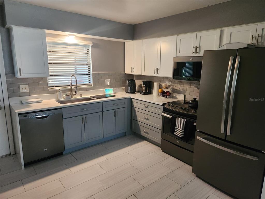 A kitchen features gray lower cabinets, white upper cabinets, stainless steel appliances, and tile flooring — 1695 N BANANA RIVER DRIVE, MERRITT ISLAND, FL