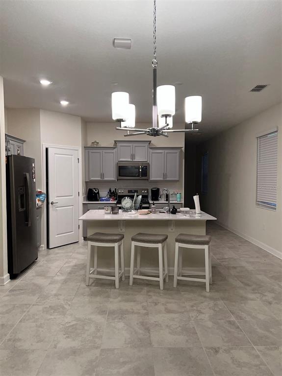 A kitchen features gray cabinets, a central island with three stools, and tile flooring — 14186 TITLE WAY, WINTER GARDEN, FL