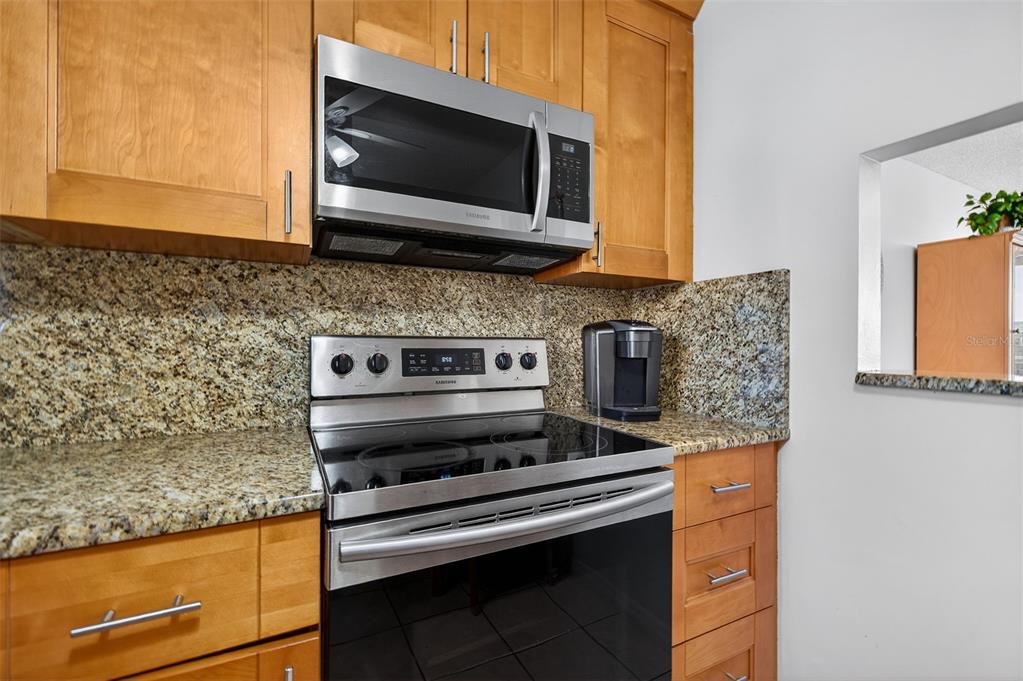 A kitchen features wood cabinets, granite countertops, and stainless steel appliances — 7625 SUN ISLAND DRIVE S UNIT 207, SOUTH PASADENA, FL