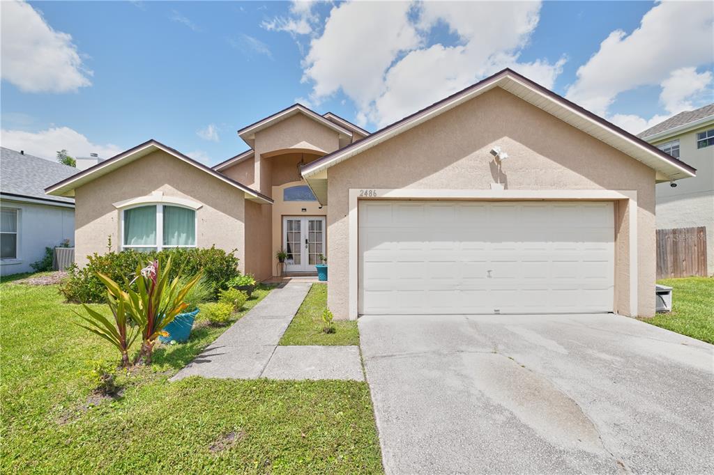 A single-story house with a beige stucco exterior, a two-car garage, and a front walkway — 2486 ISLAND CLUB WAY, ORLANDO, FL
