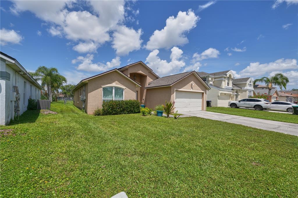 A tan, single-story suburban house with a two-car garage and a grassy front yard — 2486 ISLAND CLUB WAY, ORLANDO, FL