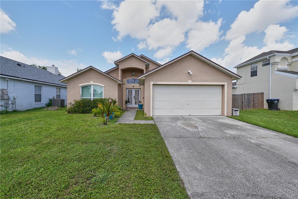 A single-story suburban house with a tan stucco exterior, a two-car garage, and a lawn — 2486 ISLAND CLUB WAY, ORLANDO, FL