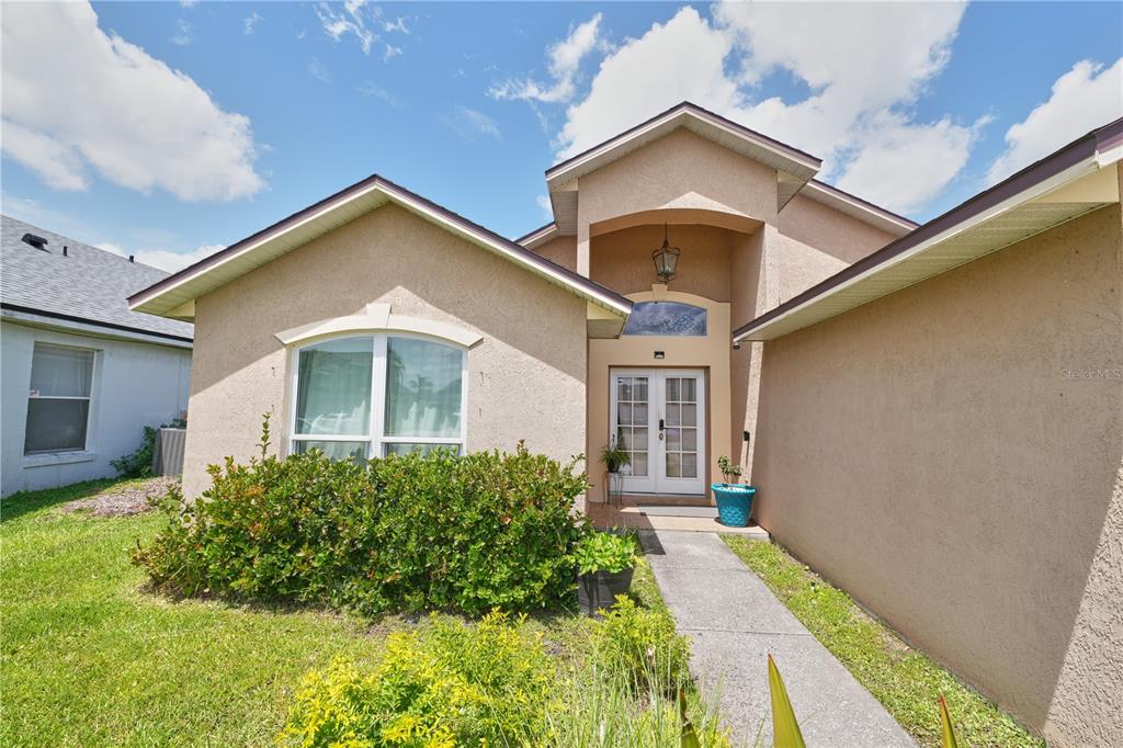 A tan stucco house features a front walkway leading to a double-door entryway — 2486 ISLAND CLUB WAY, ORLANDO, FL