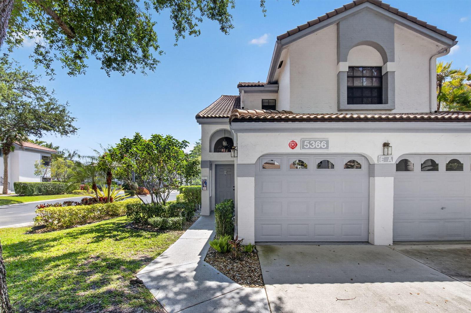 A two-story townhouse exterior features a gray garage door, a concrete walkway, and landscaping — 5366 Venetia Court, Boynton Beach FL 33437, BOYNTON BEACH, FL