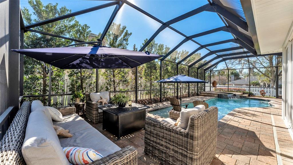 A screened-in patio features a pool, outdoor furniture, and a large blue umbrella — 2409 JENNA LN, LAKELAND, FL