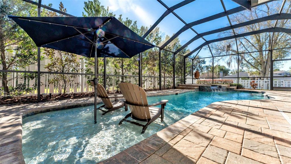 A screened-in pool area features two chairs in the shallow end under a blue umbrella — 2409 JENNA LN, LAKELAND, FL