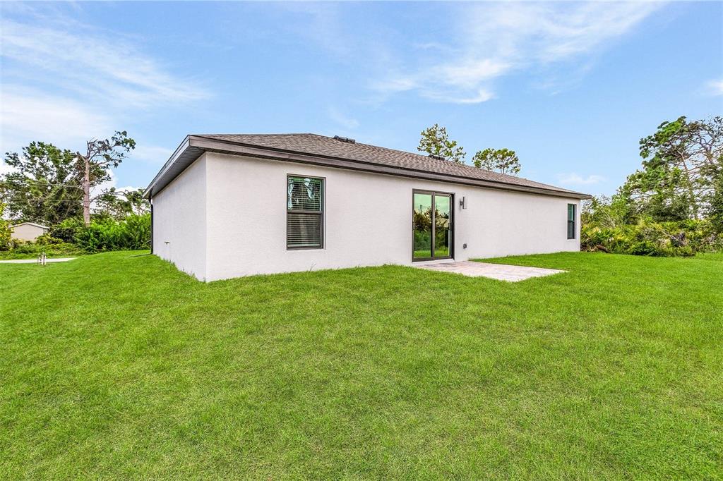 The exterior of a single-story house features a stucco finish, a sliding glass door, and windows — 6007 GILLOT BOULEVARD, PORT CHARLOTTE, FL