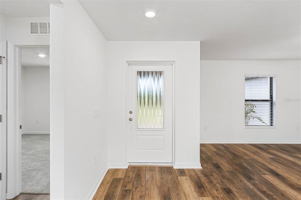 An entryway features a white front door with decorative glass, wood-look flooring, and white walls — 6007 GILLOT BOULEVARD, PORT CHARLOTTE, FL