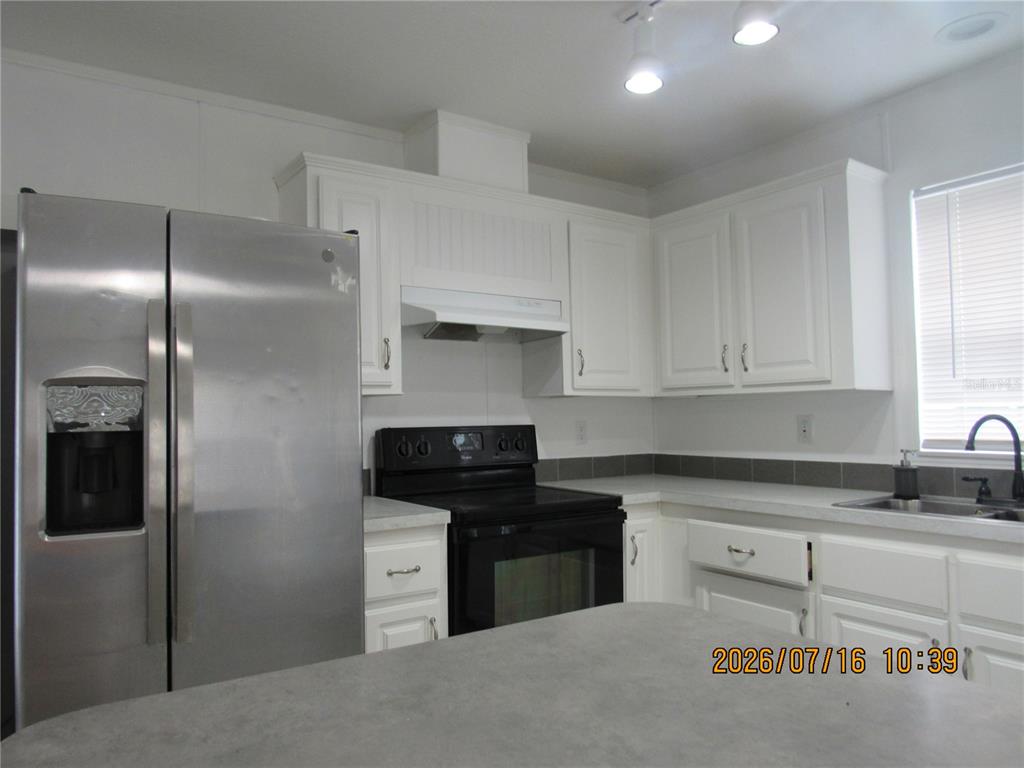 A kitchen features white cabinets, stainless steel appliances, a black stove, and gray countertops — 11719 LAKE DRIVE, CLERMONT, FL