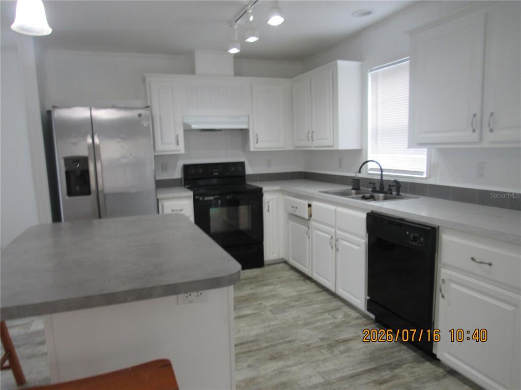 A kitchen features white cabinets, stainless steel appliances, a gray island, and wood-look flooring — 11719 LAKE DRIVE, CLERMONT, FL