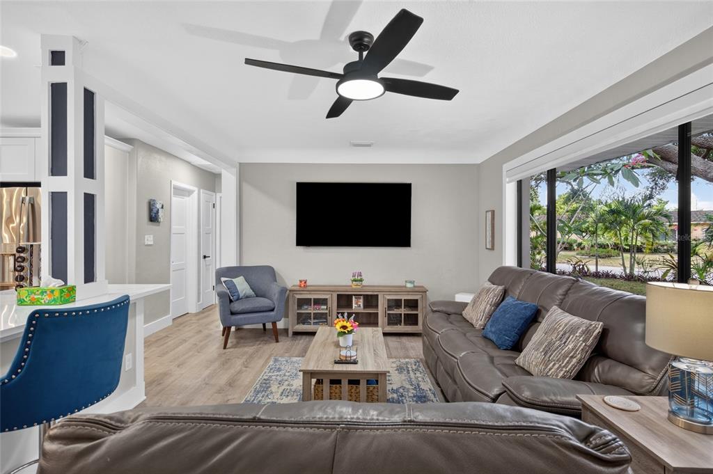 A living room features a gray sofa, a television, a ceiling fan, and large windows — 2901 70TH STREET N, ST PETERSBURG, FL