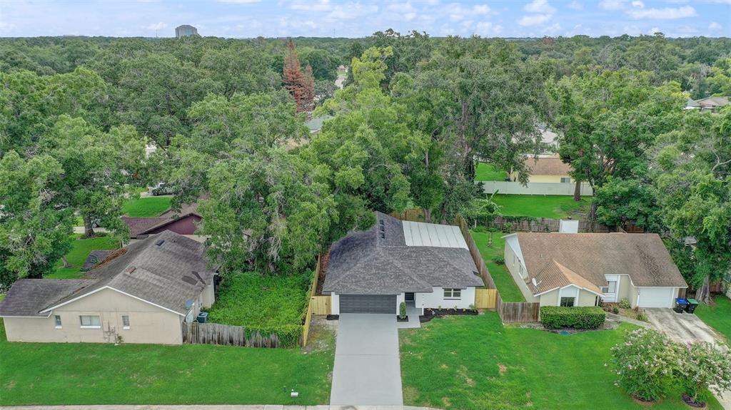 An aerial view shows three suburban houses with driveways and lawns surrounded by mature trees — 7711 LAKESIDE WOODS DRIVE, ORLANDO, FL
