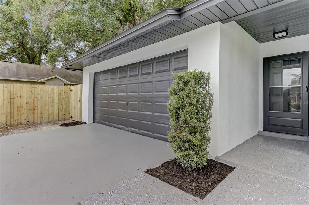A gray garage door, a front door, and a small shrub in a mulched bed — 7711 LAKESIDE WOODS DRIVE, ORLANDO, FL