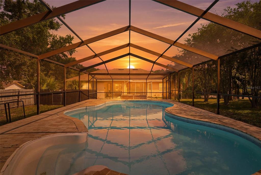 A swimming pool with a screened enclosure sits in a backyard at sunset — 10110 BRIAR CIRCLE, HUDSON, FL