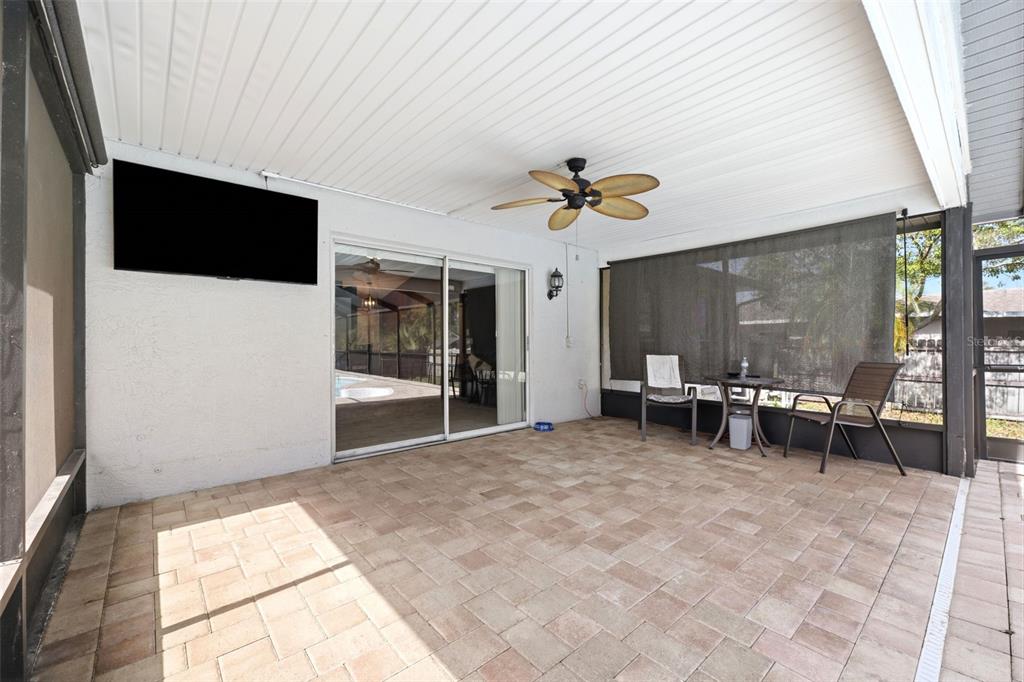 A covered patio features a paved floor, a ceiling fan, a wall-mounted television, and sliding doors — 10110 BRIAR CIRCLE, HUDSON, FL