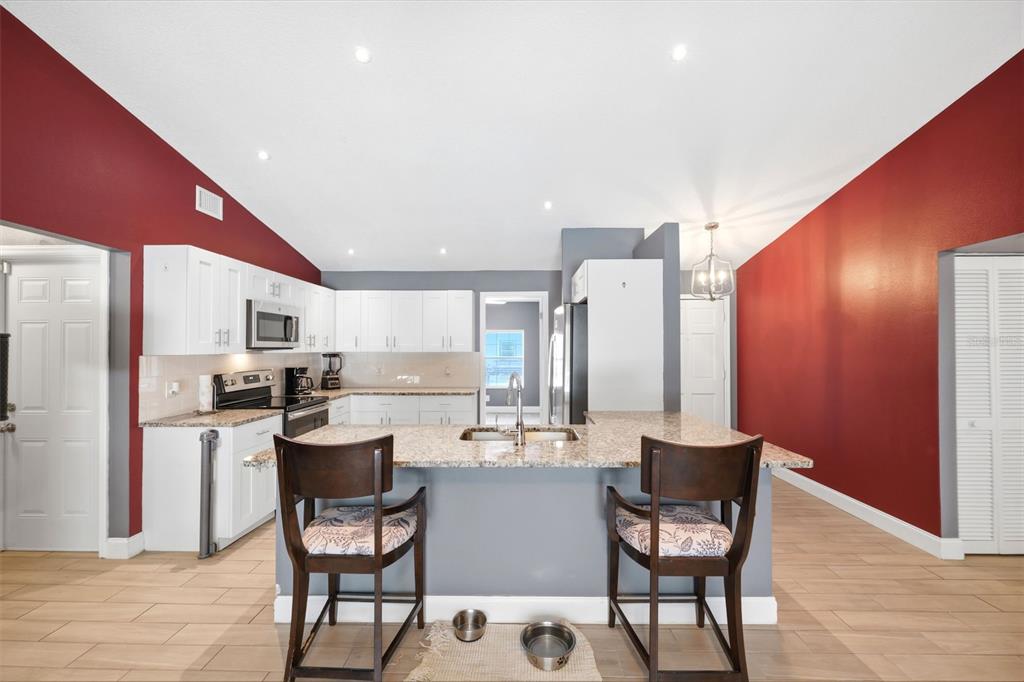 A kitchen features white cabinets, granite countertops, a central island with bar stools, and red walls — 10110 BRIAR CIRCLE, HUDSON, FL