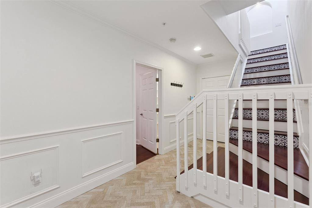 A white hallway features a herringbone floor, wainscoting, and a staircase with patterned tile risers — 1650 PROSPECT AVENUE, ORLANDO, FL