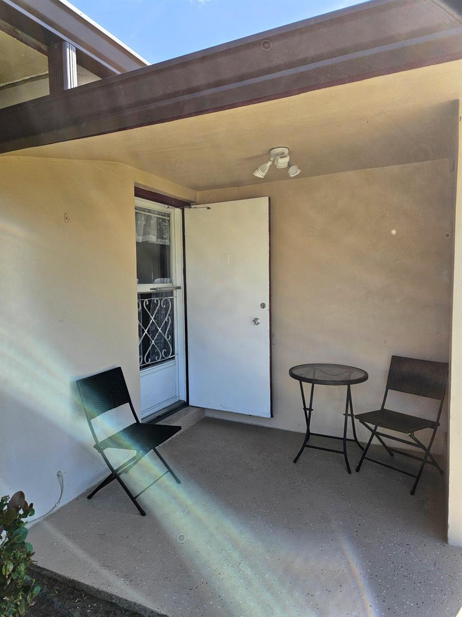 A covered patio features a white door, two black chairs, and a small round table — 2950 Crosley Drive E # C, West Palm Beach FL 33415, WEST PALM BEACH, FL