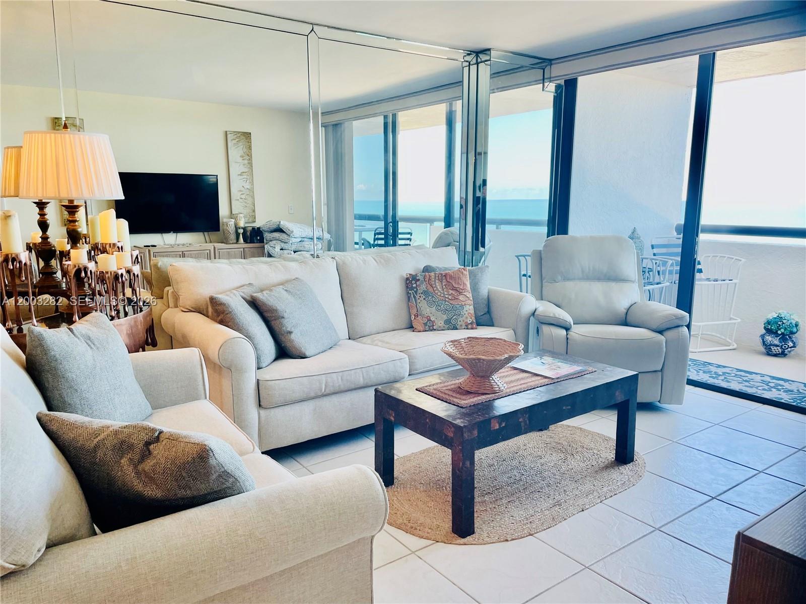 A living room with a beige sofa, armchair, coffee table, and a balcony overlooking the ocean — 2555 Collins Ave # 1805, Miami Beach FL 33140, MIAMI BEACH, FL