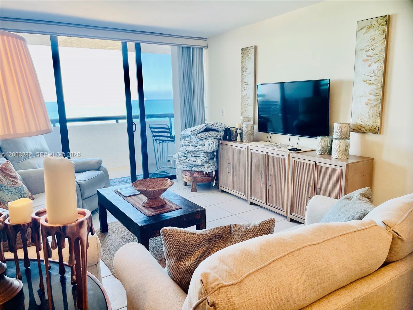 A living room features a television, a light-colored sofa, and a balcony with ocean views — 2555 Collins Ave # 1805, Miami Beach FL 33140, MIAMI BEACH, FL