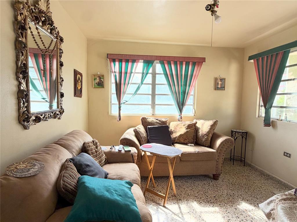 A living room features two beige sofas, a decorative mirror, and windows with patterned curtains — 156 Km 0.7 PUEBLO, OROCOVIS, PR