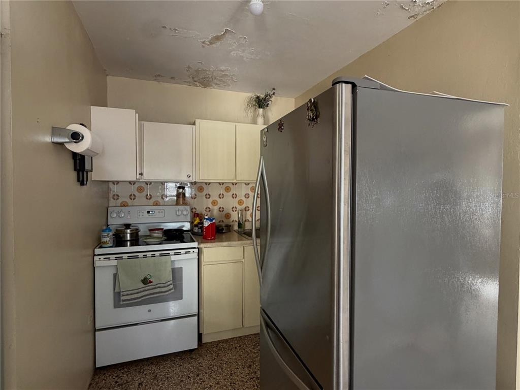 A small kitchen features white cabinets, a white stove, a stainless steel refrigerator, and damaged ceiling — 156 Km 0.7 PUEBLO, OROCOVIS, PR