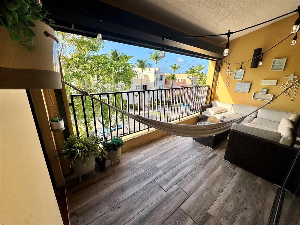 A balcony features wood-look tile flooring, a hammock, wicker seating, and string lights — 100 CANDELERO DRIVE UNIT 2067, HUMACAO, PR