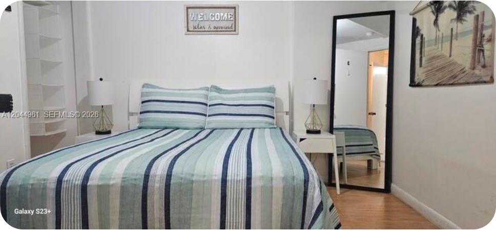 A bedroom features a bed with striped bedding, two nightstands with lamps, and a floor mirror — 144 NW 7th Ave # 1, Dania Beach FL 33004, DANIA BEACH, FL