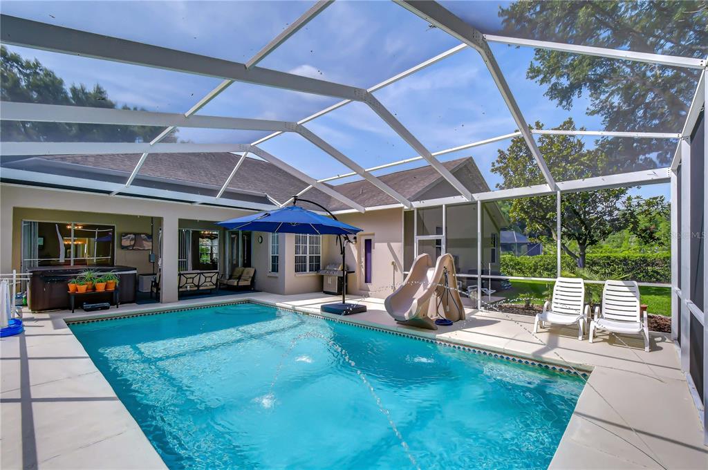 A screened-in swimming pool area with a slide, hot tub, and patio furniture — 4916 WILLOW RIDGE TERRACE, VALRICO, FL