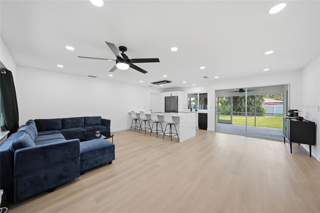An open-concept living room and kitchen with light wood floors, white walls, and sliding doors — 2506 LAKESHORE CIRCLE, PORT CHARLOTTE, FL
