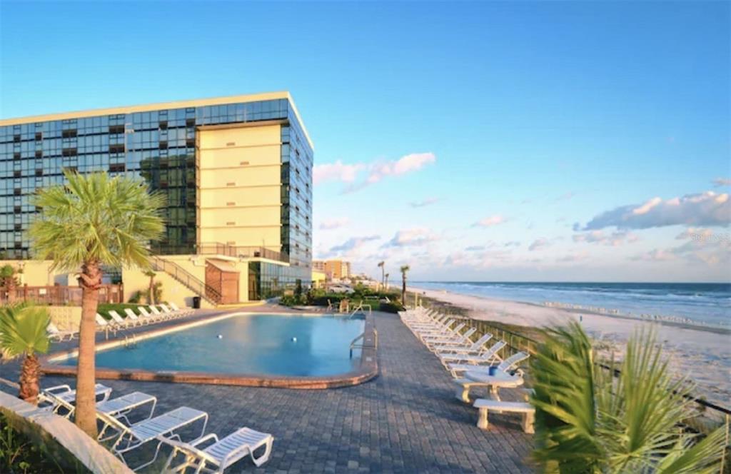 A swimming pool sits on a paved patio next to a multi-story building and beach — 1909 S ATLANTIC AVENUE UNIT 520 & 521, DAYTONA BEACH, FL