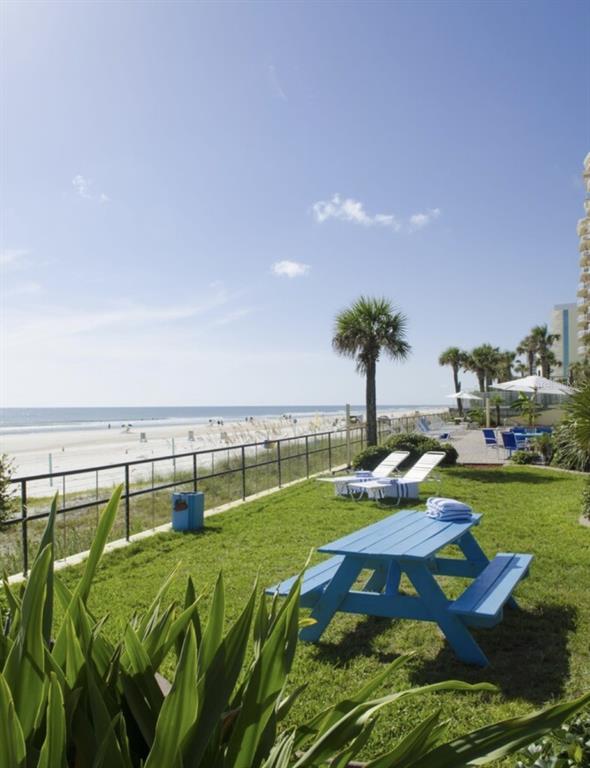 A blue picnic table sits on a grassy lawn overlooking a sandy beach and ocean — 1909 S ATLANTIC AVENUE UNIT 520 & 521, DAYTONA BEACH, FL