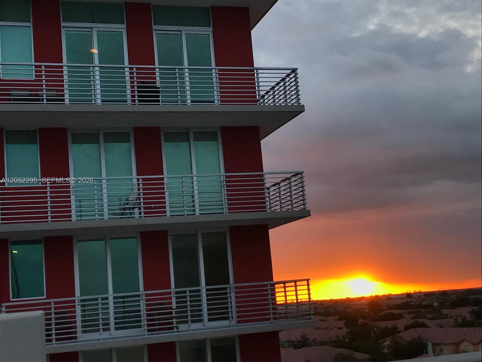 A red apartment building exterior features multiple balconies overlooking a sunset over a residential area — 7875 NW 107th Ave # 812, Doral FL 33178, DORAL, FL