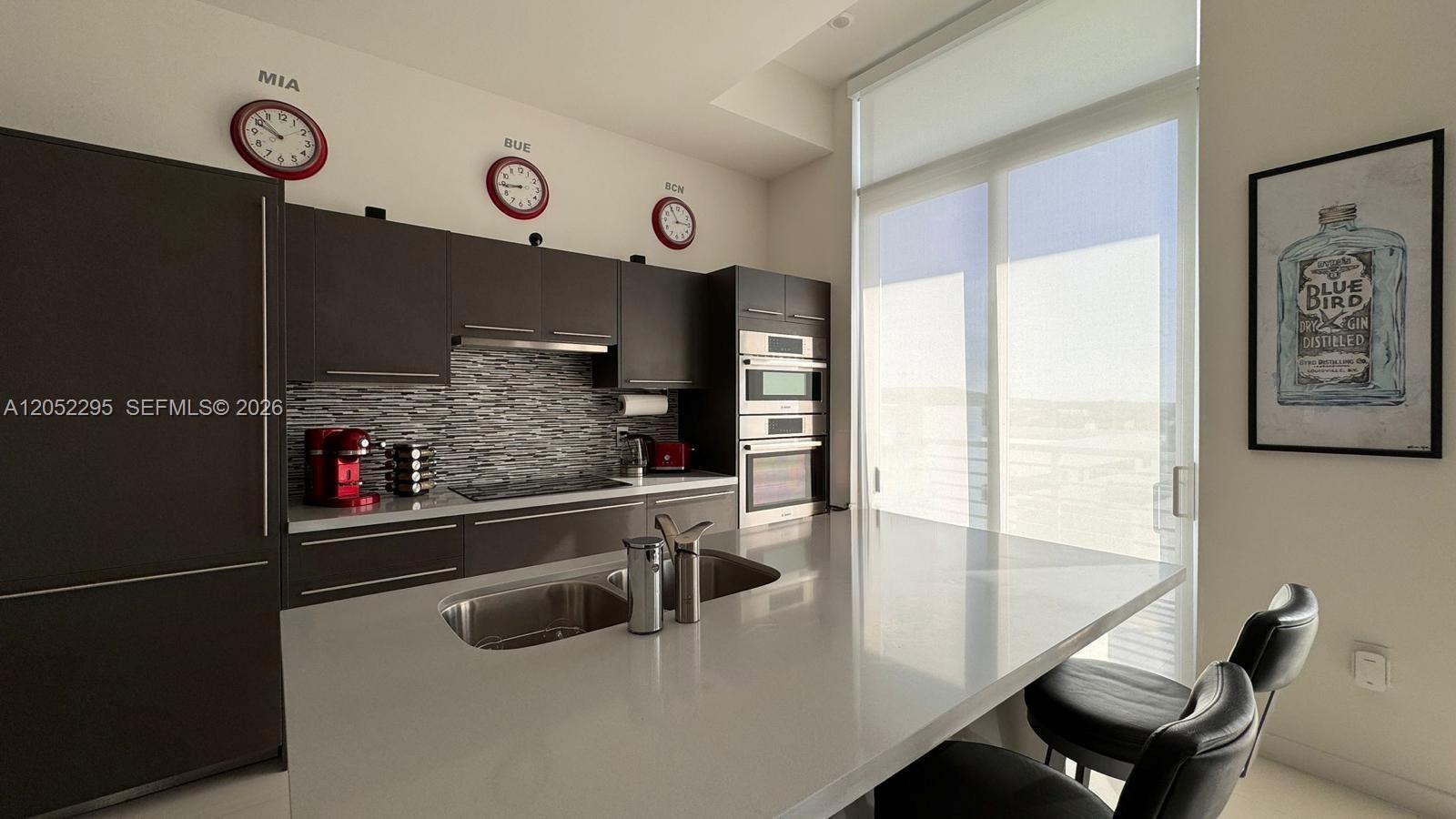 A modern kitchen features dark cabinetry, a quartz island with a sink, and wall clocks — 7875 NW 107th Ave # 812, Doral FL 33178, DORAL, FL