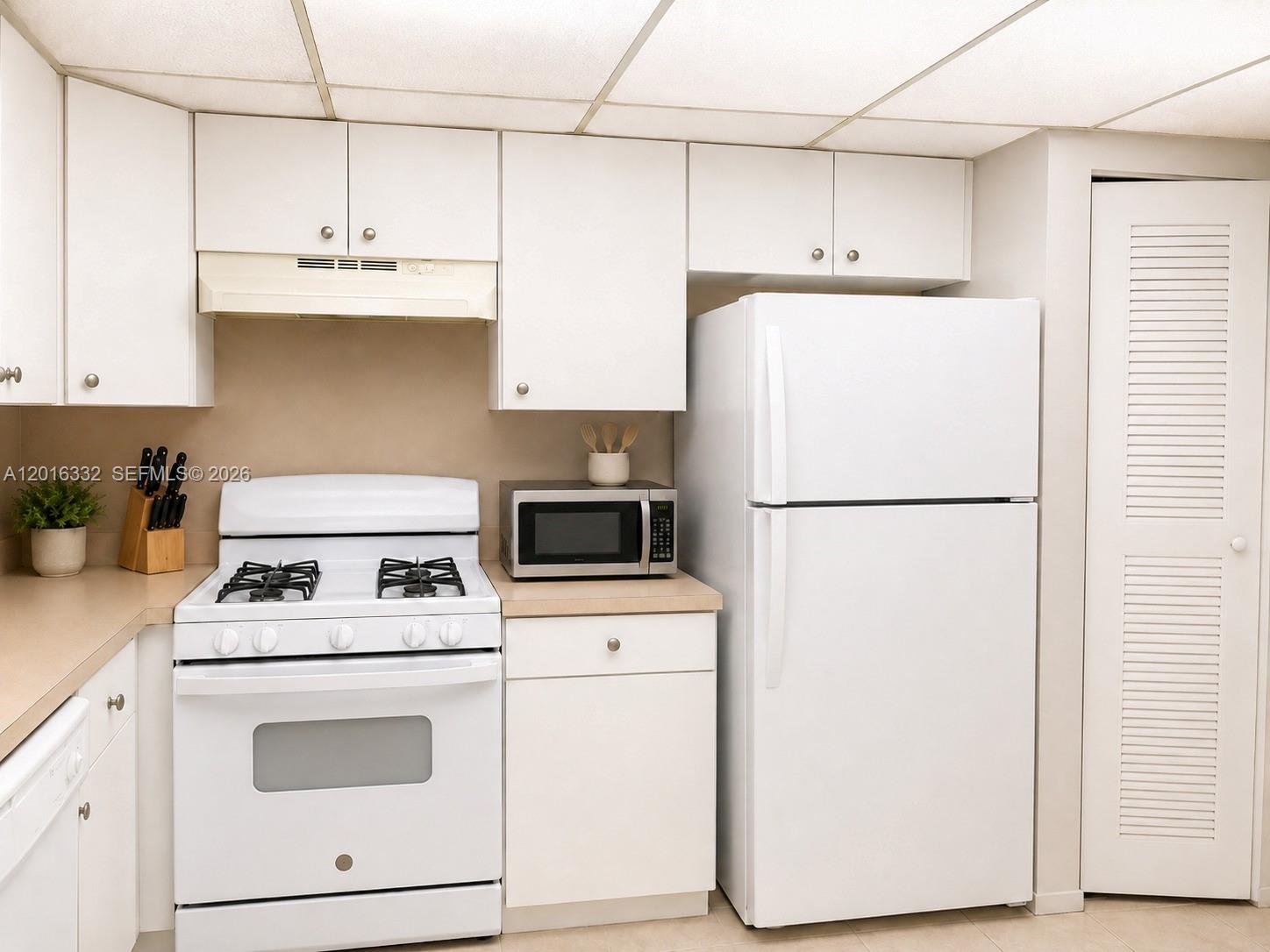 A kitchen features white cabinets, a gas stove, a microwave, and a white refrigerator — 17911 NW 68th Ave # M201, Hialeah FL 33015, HIALEAH, FL